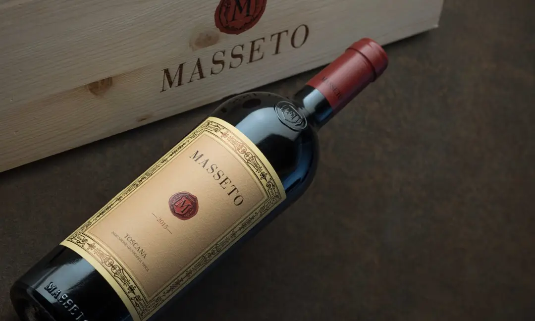 Bottle of Masseto 2015 wine placed on a dark surface next to a personalized wooden box, highlighting the elegant and luxurious label of the renowned Tuscan wine 