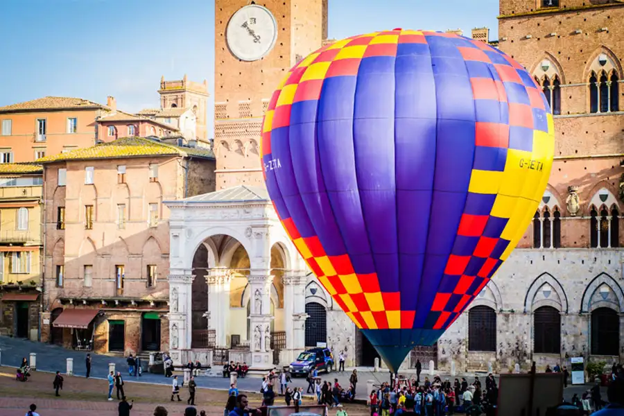 Colorful hot air balloon set up in Piazza del Campo, in Siena, with historic buildings and the Torre del Mangia in the background