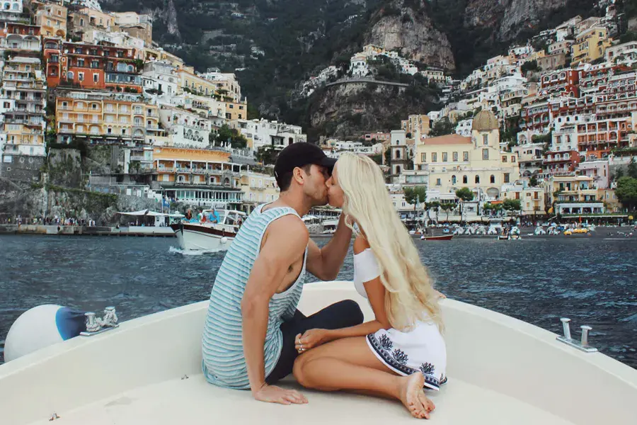 Couple kissing at the bow of a boat in front of the colorful village of Positano, on the Amalfi Coast, during a romantic sea tour.