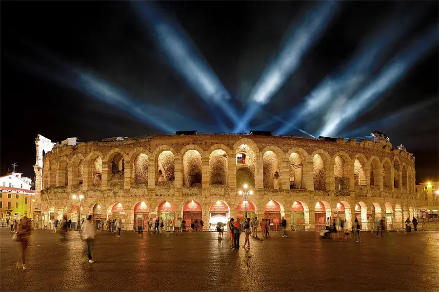 Arena di Verona illuminated at night with beams of light in the sky, before an opera festival performance in Italy.