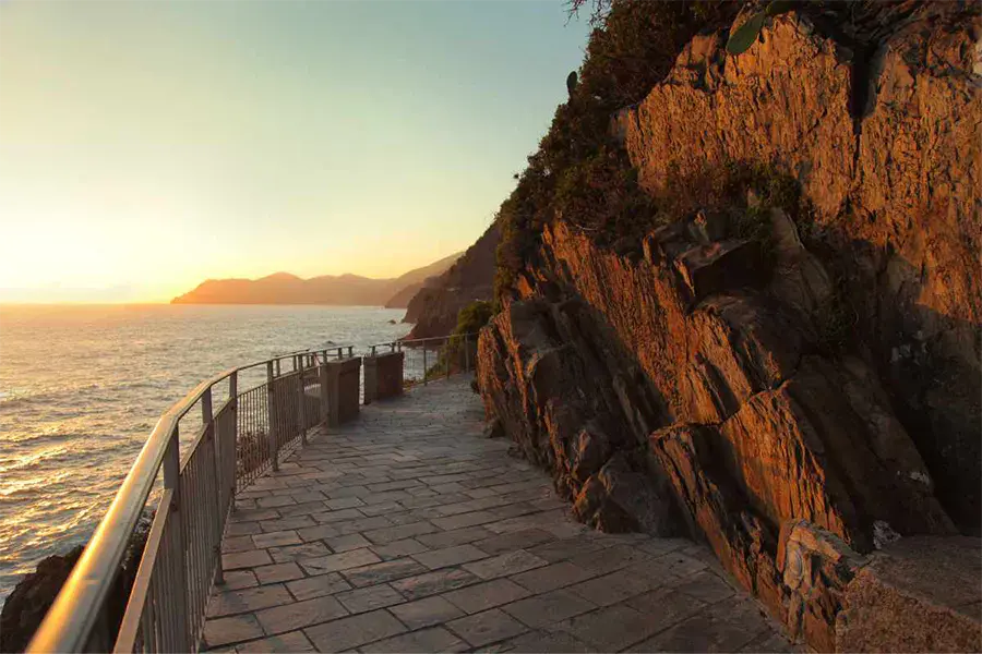 Via dell’Amore trail in Cinque Terre, with a view of the sea at dusk and the rocky cliff illuminated by the golden light of sunset.