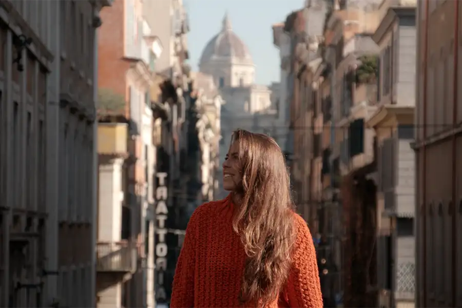 Smiling woman walking through a historic street in Florence with the dome of the Cathedral in the background.