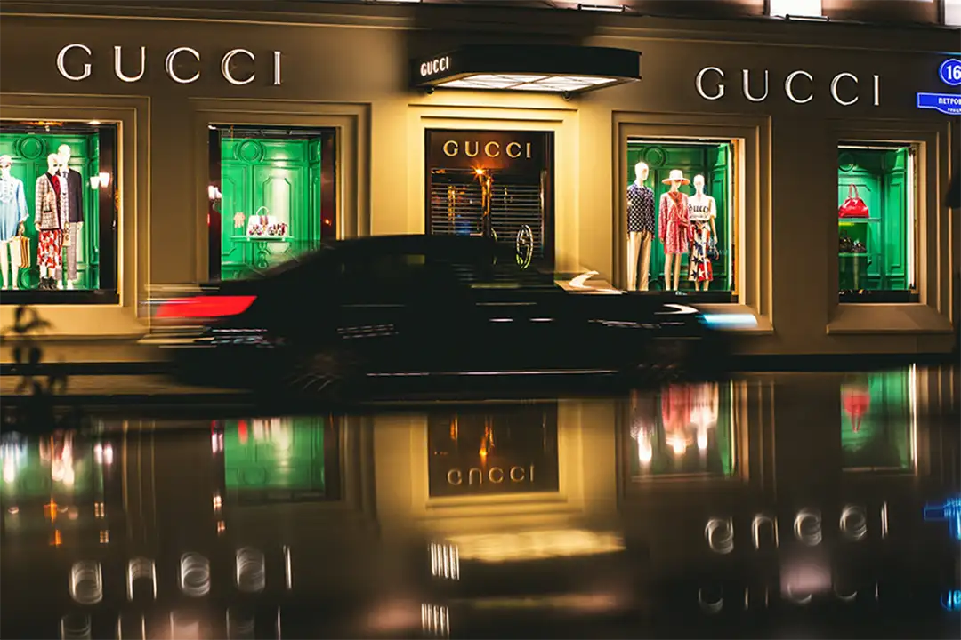 Gucci store window lit at night, showcasing elegant outfits that highlight the luxury of modern Italian fashion.
