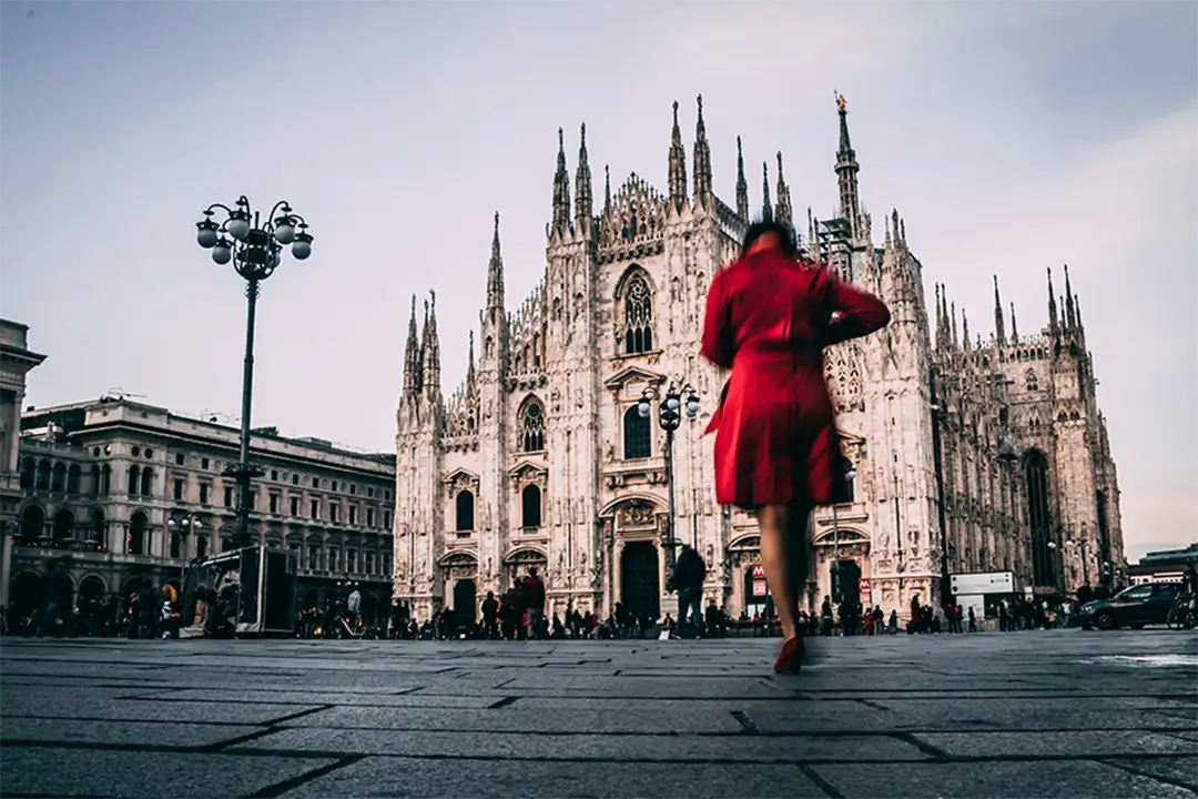 Woman in red dress walking in front of Milan’s Duomo, blending iconic architecture with the elegance of Italian fashion.
