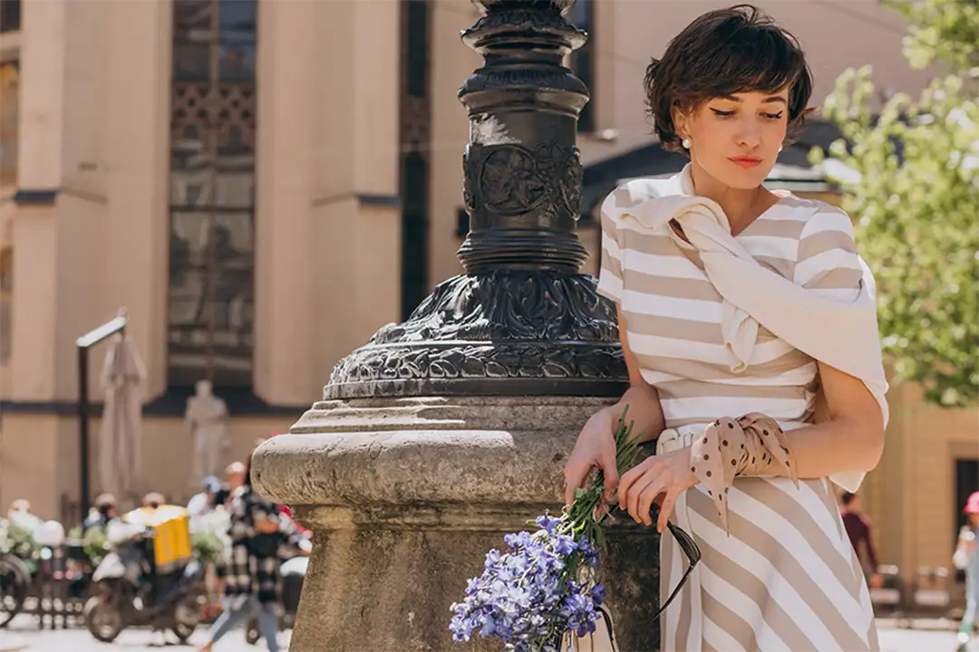 Woman in striped dress holding flowers on a classic Italian street, expressing the charm and femininity of Italian fashion.
