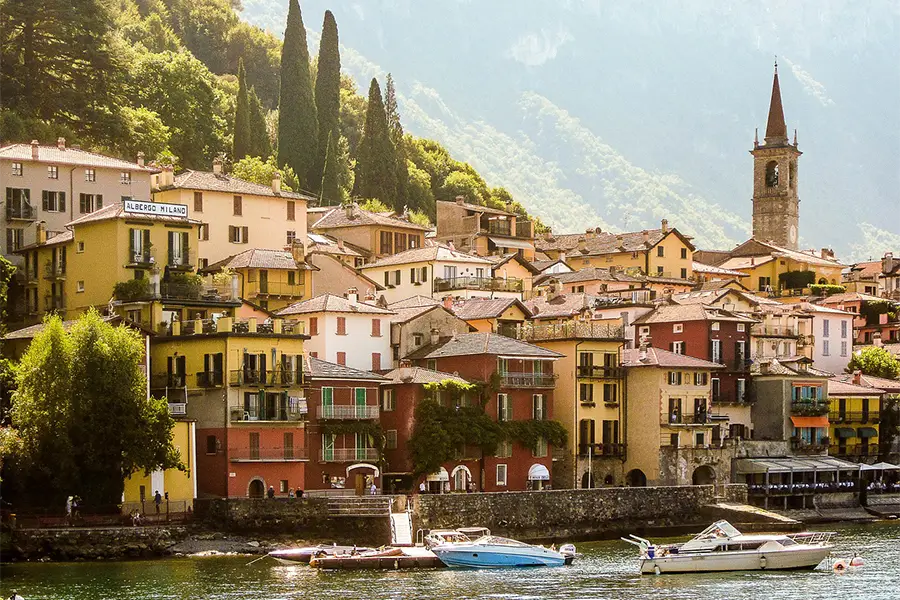 Lakeside village on Lake Como with boats docked at the pier, an ideal setting for boat tours in Italy among mountains and charming architecture
