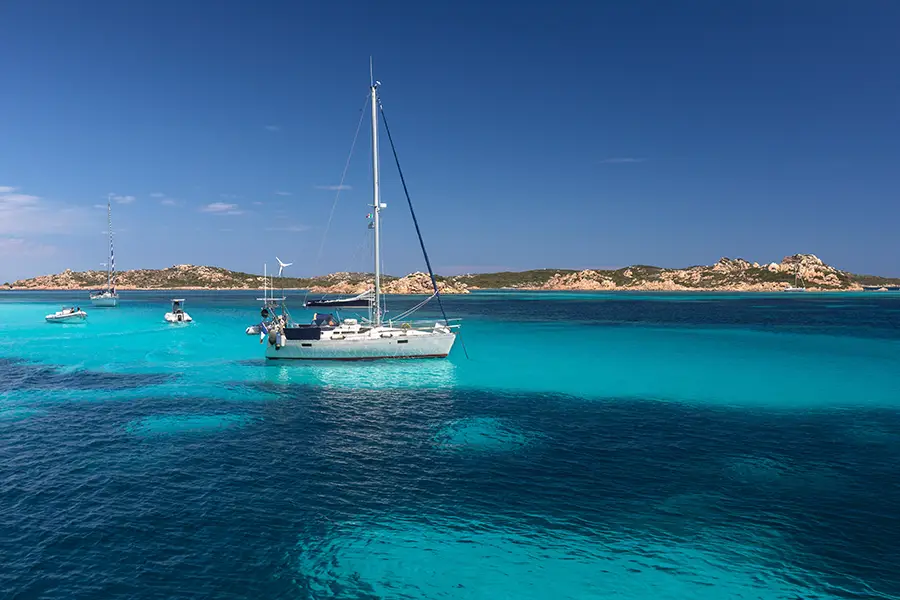 Barcos flutuando sobre as águas azul-turquesa da Sardenha, destino perfeito para passeios de barco na Itália com cenários paradisíacos.