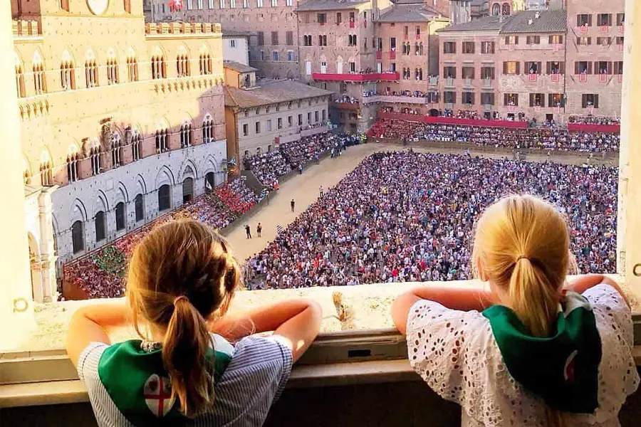 Two children watching the crowd gathered in Piazza del Campo to see the historic Palio di Siena horse race.
