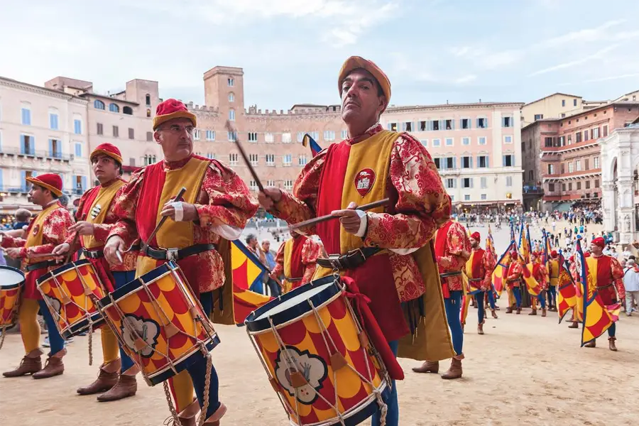 Musicians in historical costumes parading with drums in Piazza del Campo, honoring the tradition of the Palio di Siena.