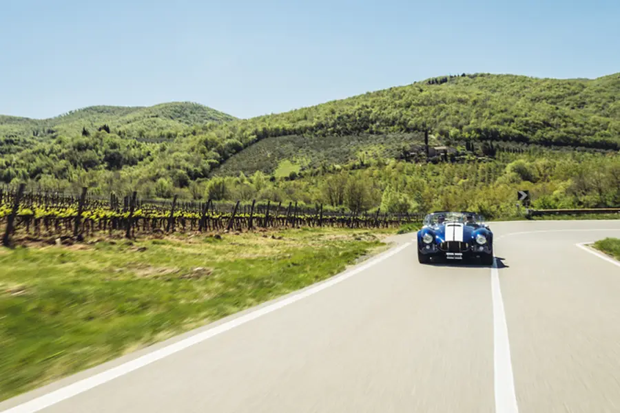 Classic sports car driving along a winding road through vineyards and green hills on the Chiantigiana route in Tuscany, Italy