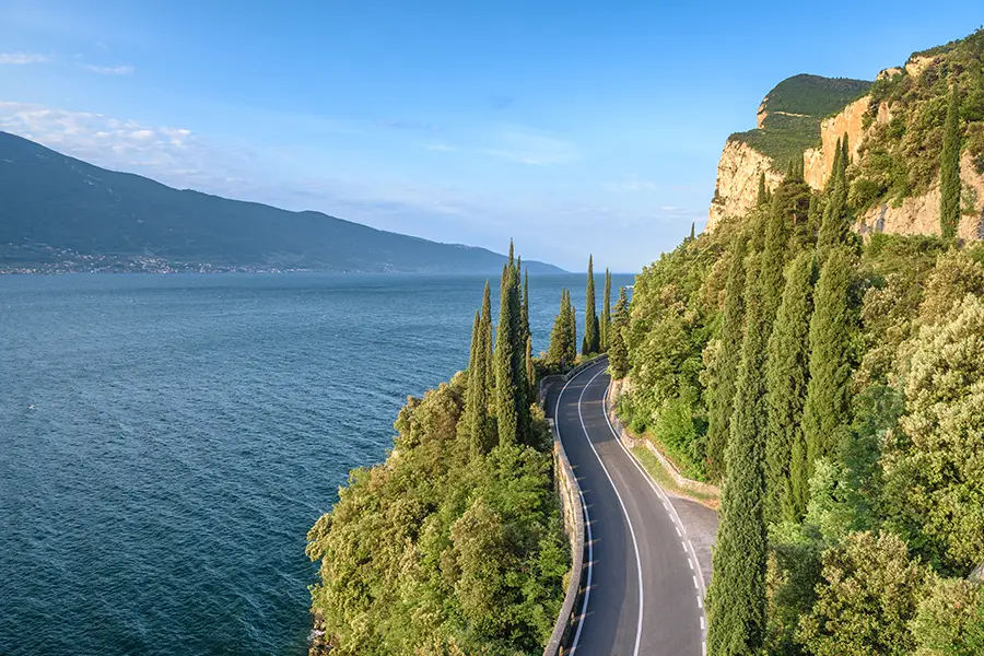 Scenic road Via Gardesana Occidentale along Lake Garda with cliffs, cypress trees, and mountains in the background